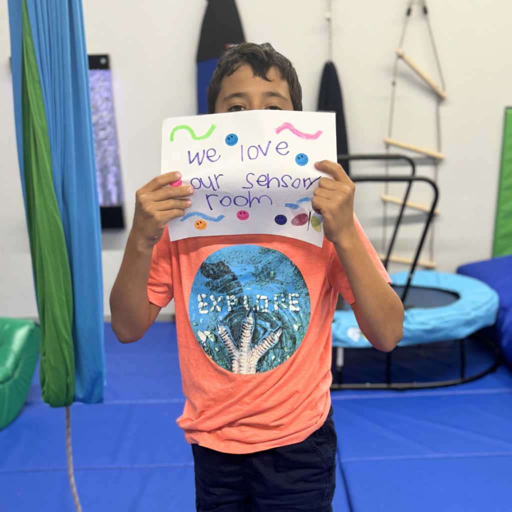 PEEP student holding up a handmade sign that says "We love our sensory room"