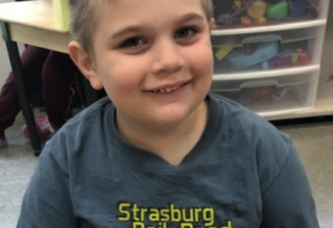 Young boy smiling wearing a gray shirt in school